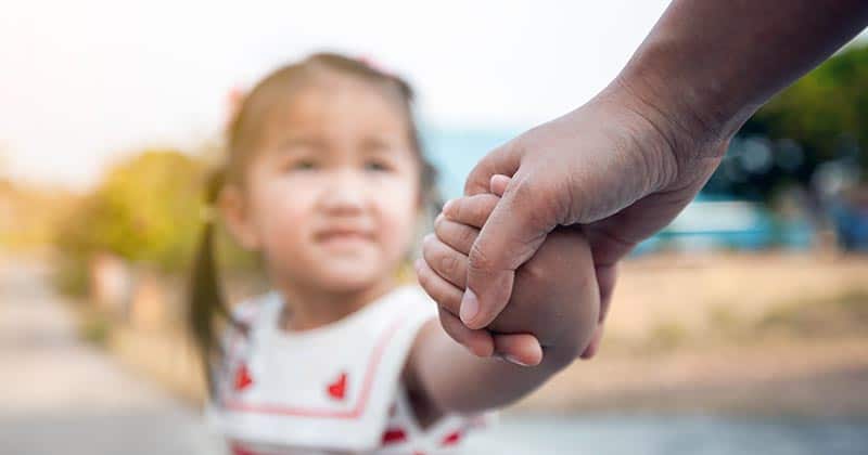 Parent taking the hand of a toddler girl.