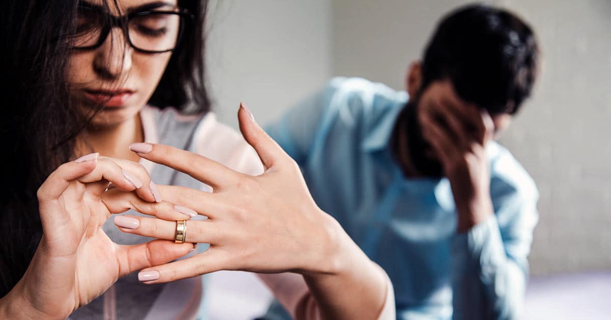 Woman taking wedding ring off finger with man in background